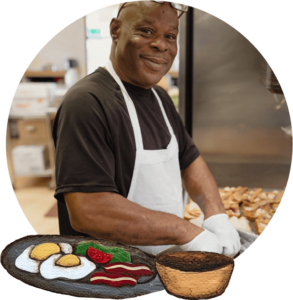 Man in a commercial kitchen preparing a large batch of sandwiches.